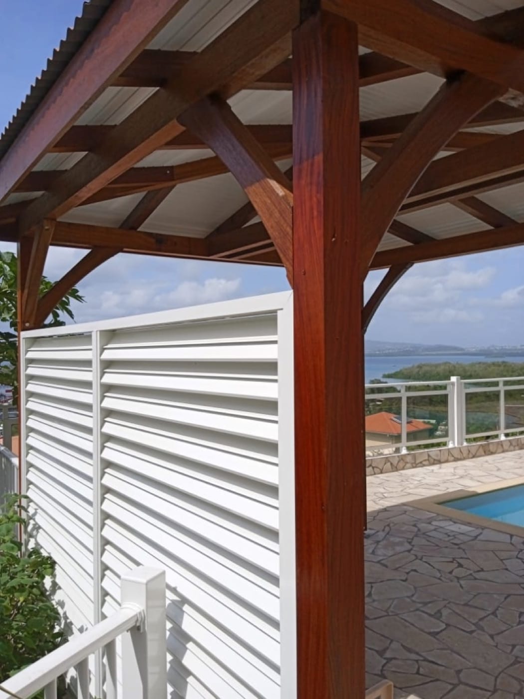 Carbet en bois traditionnel couvert en tôle au-dessus d'une terrasse avec piscine en Martinique